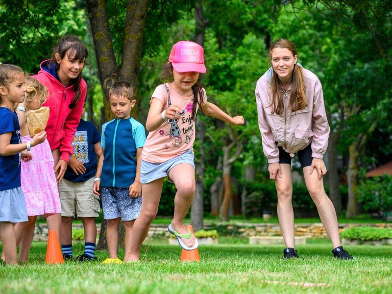 Kinder spielen draußen auf einer Wiese mit einem Holzball, umgeben von Bäumen.