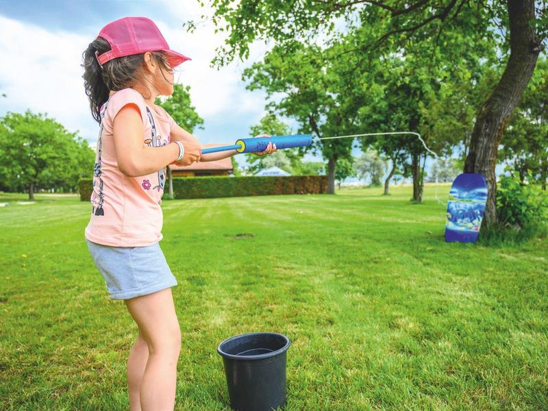 Kind schießt mit Wasserpistole auf Ziel an Baum im Park