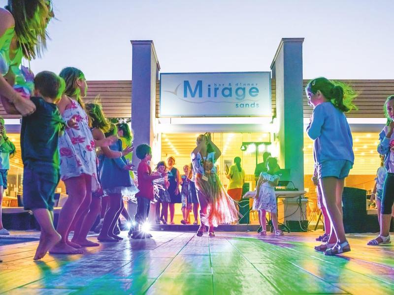Kinder spielen auf einer bunten Tanzfläche mit beleuchtetem Mirabe-Schild im Hintergrund.