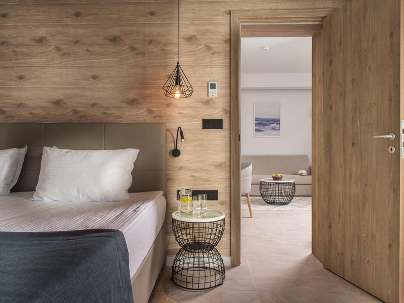 Modernes Hotelzimmer mit Holzverkleidung, großem Bett und Blick in den angrenzenden Raum.