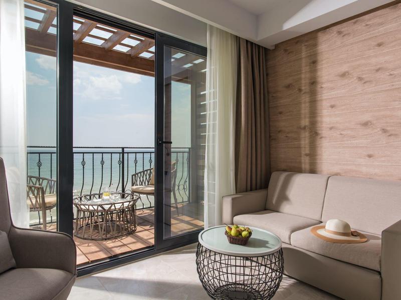 Modernes Hotelzimmer mit Balkon und Meerblick, gemütlicher Sitzecke und Holzdekor.