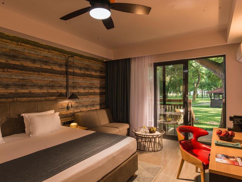 Modernes Hotelzimmer mit Doppelbett, Holzakzenten und Blick auf einen grünen Garten.