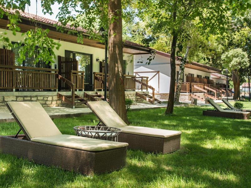 Sonnenliegen auf grünem Gras vor Bungalows unter Bäumen an einem sonnigen Tag.