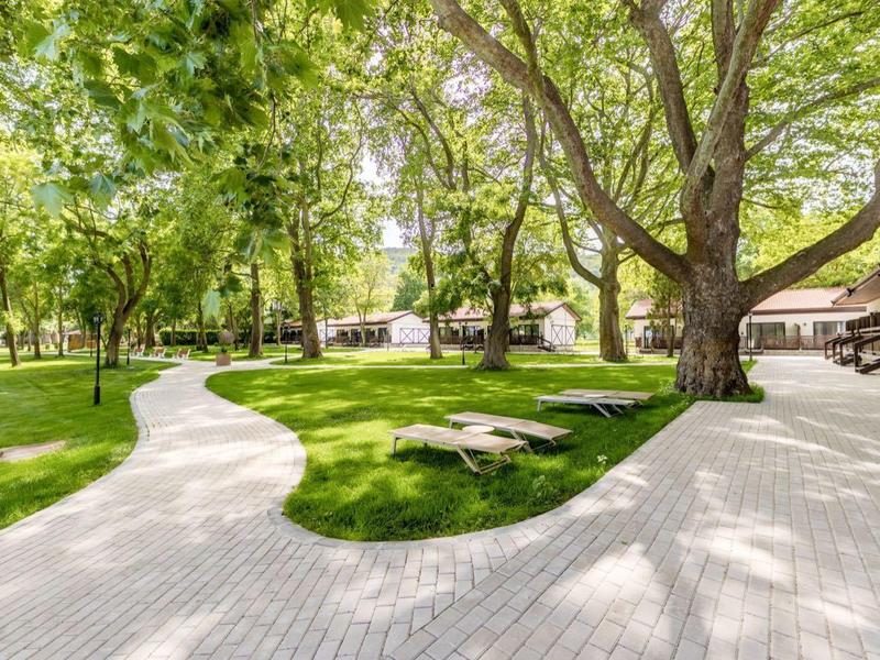 Parkanlage mit geschwungenem gepflastertem Weg und Bäumen neben einem Hotelgebäude.