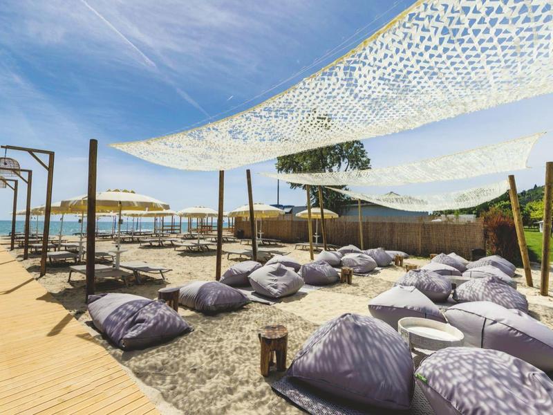 Outdoor-Lounge-Bereich am Strand mit Sitzsäcken und Sonnensegeln über Sandboden.