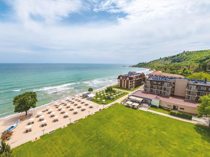 Großes Hotel an einem grünen Hang mit Blick auf den Strand und das Meer unter blauem Himmel.