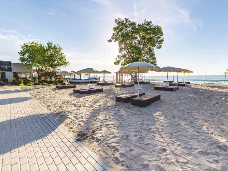 Freizeitbereich mit Sonnenliegen und Schirmen am Wasser bei klarem Himmel.