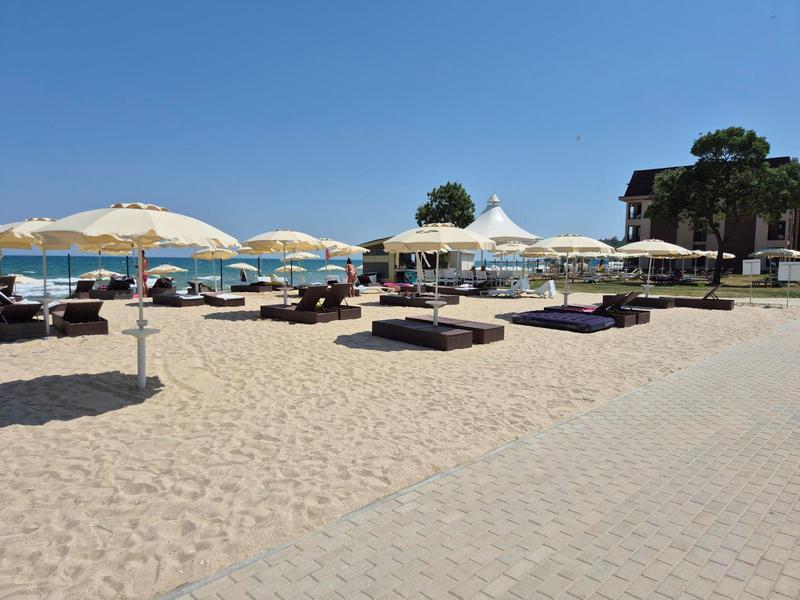 Sandstrand mit Sonnenschirmen, Liegen und Blick auf das blaue Meer bei klarem Himmel.