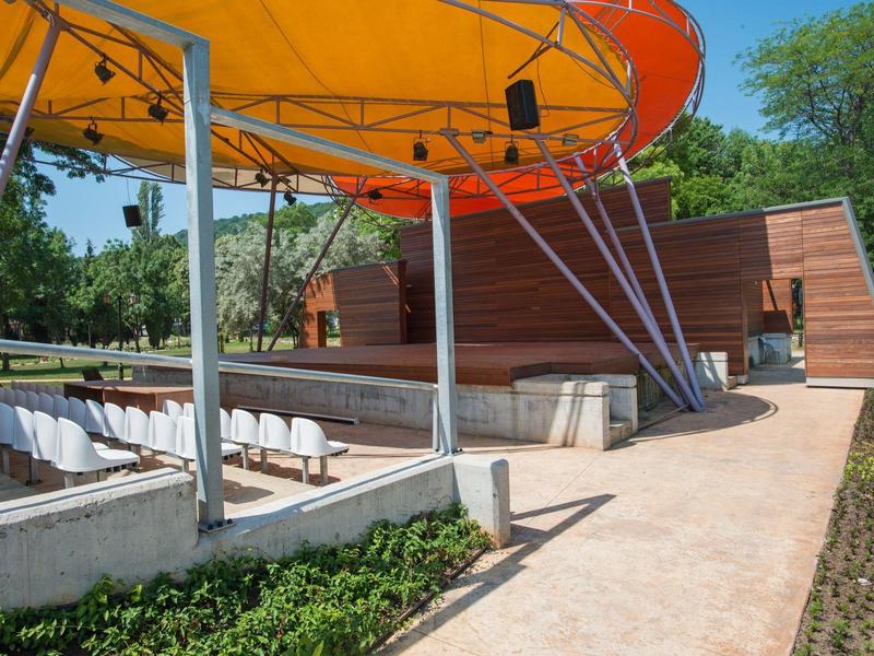 Freiluftbühne mit oranger Überdachung und Sitzreihen im Gartenbereich eines Hotels.