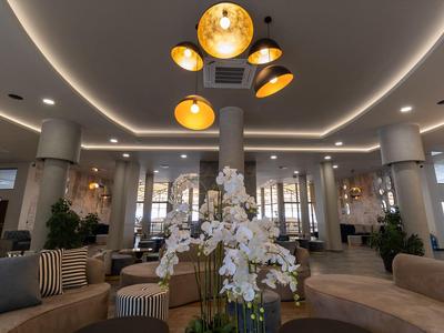 Elegancka część wypoczynkowa hotelu z okrągłymi miejscami do siedzenia, kwiatową dekoracją i nowoczesnym oświetleniem sufitowym.