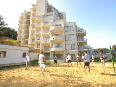 Ludzie grają w siatkówkę na piaszczystym boisku przed wielopiętrowym budynkiem hotelu pod czystym niebem.