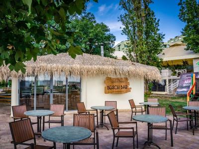 Lege buitenzitruimte met tafels en stoelen voor een gebouw met een rieten dak en bord 'Süßbar'.