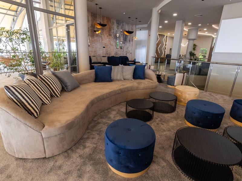 Gezellig zithoek met gebogen bank, kleurrijke kussens en blauwe krukjes in een modern hotel.