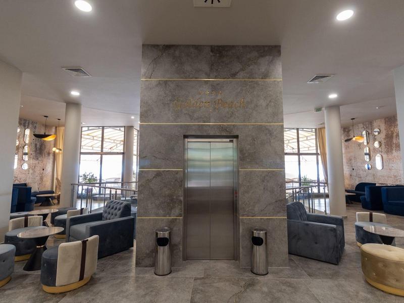 Moderne hotel lobby met lift in het midden, zitgedeeltes en grote ramen op de achtergrond.