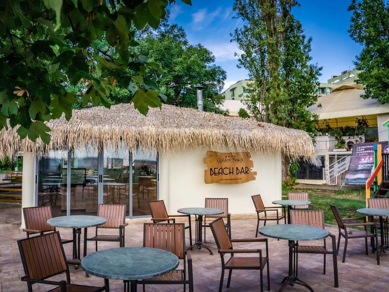 Lege buitenzitruimte met tafels en stoelen voor een gebouw met een rieten dak en bord 'Süßbar'.