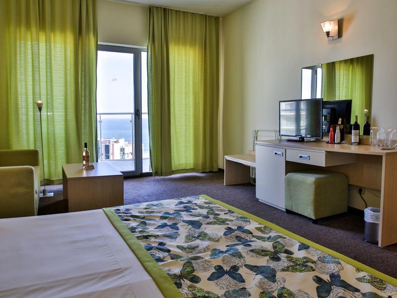 Lichte hotelkamer met groene accenten, zithoek en zeezicht door de balkondeur.