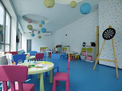 Kleurrijke speelkamer voor kinderen met tafels, stoelen en dartbord in een lichte ruimte.