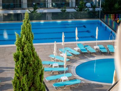 Moderní venkovní bazén s modrými lehátky a bílými slunečníky na hotelové terase.