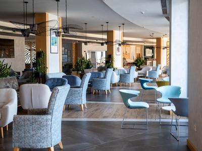 Elegantní jídelní prostor s různými židlemi a stoly v neutrálních tónech a dřevěnou podlahou.