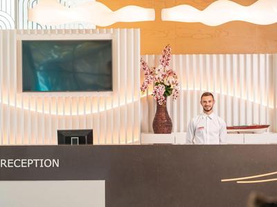 Recepce s usměvavým recepčním, moderním designem a bílým osvětlením.