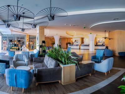 Moderní hotelová lobby s pohodlnými křesly, rostlinami a světlým dřevěným dekorem.