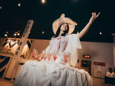 Femme en robe élégante avec chapeau servant des boissons dans un bar.
