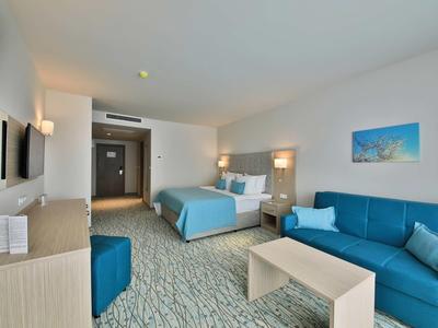 Modern hotelkamer met tweepersoonsbed, bank en lichte houten meubels.