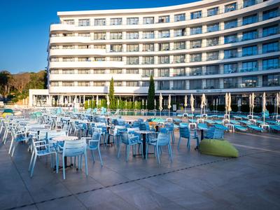 Complexe hôtelier moderne avec de nombreuses tables et chaises extérieures sur une grande terrasse par temps ensoleillé.