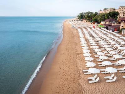 Široká písečná pláž s řadami bílých lehátek a slunečníky vedle klidného moře.