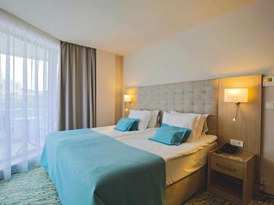 Moderne hotelkamer met twee bedden, blauw beddengoed en groot raam met gordijnen.