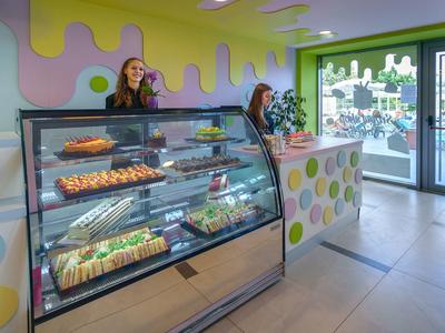 Interiér moderní pekárny s vitrínou plnou pečiva a dvěma zaměstnankyněmi za pultem.