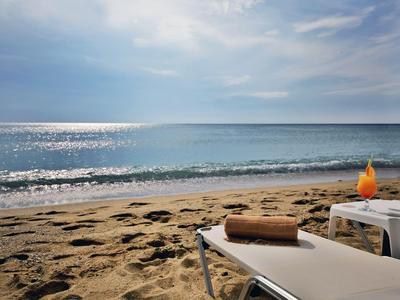 Chaise longue vide et boisson sur plage ensoleillée avec mer calme en arrière-plan.