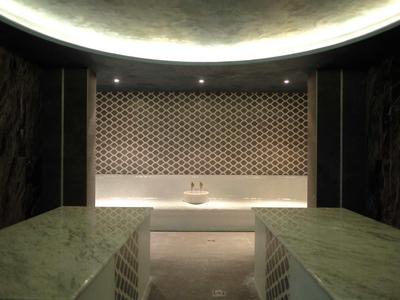 Modern hammam met marmeren banken en verlicht plafondlicht.