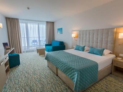 Modern ingerichte hotelkamer met tweepersoonsbed, bank en balkon met uitzicht op zee.