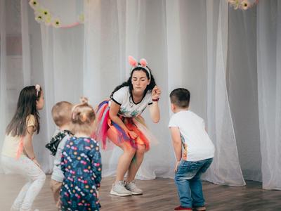 Žena s králičími ušima baví čtyři děti v světlé místnosti s bílými závěsy.