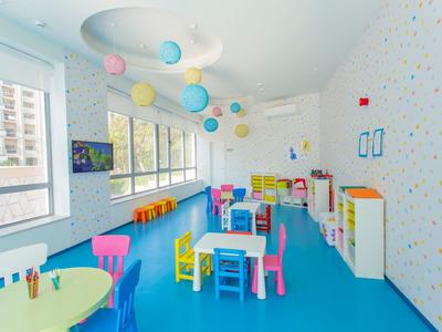 Barevná dětská herna se stoly, židlemi a oknovou zdí v jasné místnosti.