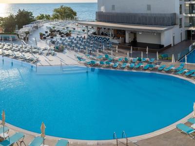 Grande piscine ronde d'hôtel avec chaises longues et parasols à côté d'un bâtiment moderne.