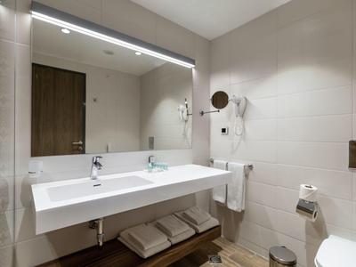 Moderní koupelna s dvojitým umyvadlem, velkým osvětleným zrcadlem a bílými dlaždicemi