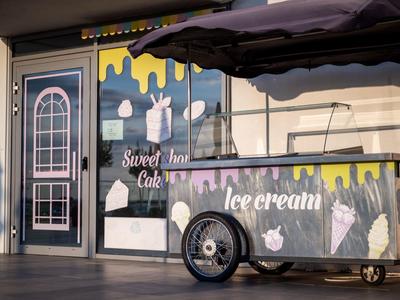 Stánek s nanuky před obchodem s barevnými cedulemi a slunečníkem