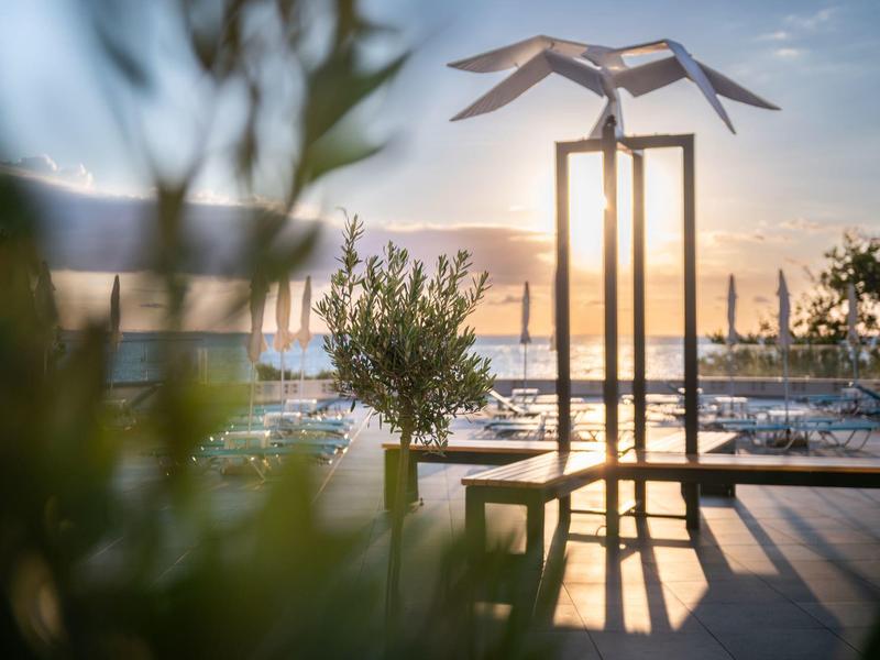 Moderní socha na terase s výhledem na přístav za západu slunce.