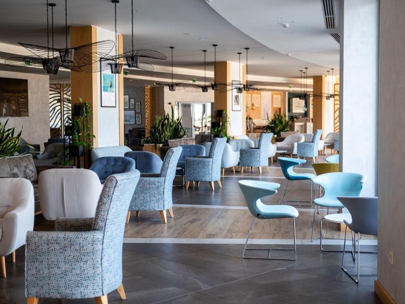 Elegantní jídelní prostor s různými židlemi a stoly v neutrálních tónech a dřevěnou podlahou.