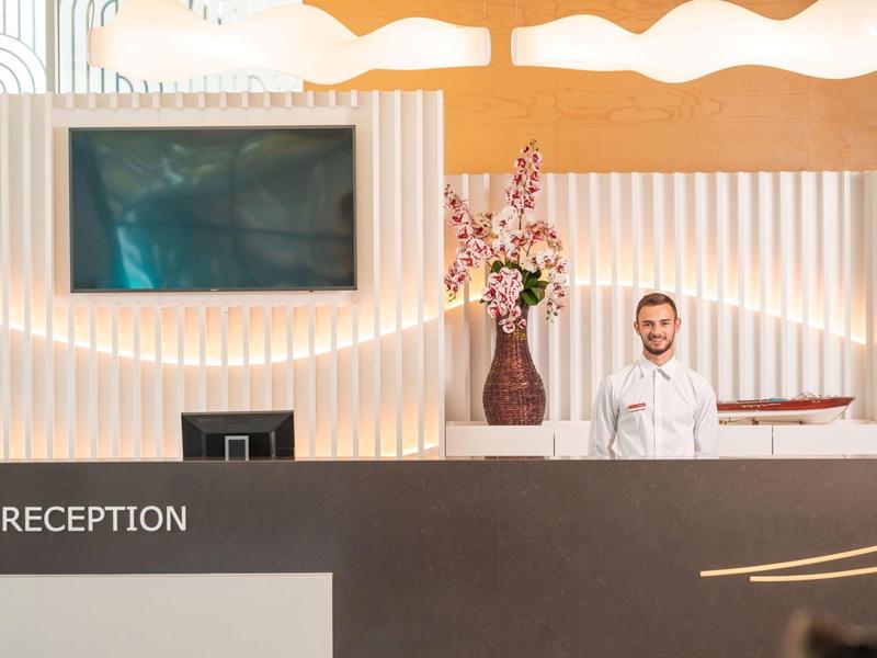 Recepce s usměvavým recepčním, moderním designem a bílým osvětlením.