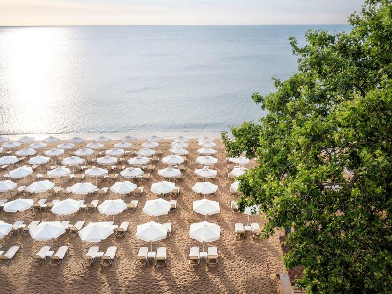 Pláž s bílými slunečníky a lehátky u moře na slunečním světle