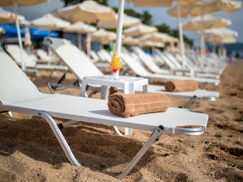 Ligstoel met handdoek en drankje op zandstrand onder parasols.