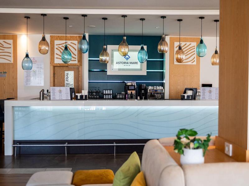 Moderně zařízený hotelový bar s světle modře osvětleným pultem a zavěšenými žárovkami.