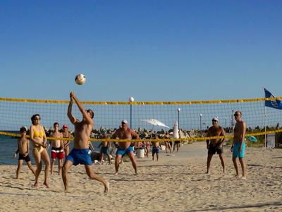 Menschen spielen Beachvolleyball auf einem sandigen Volleyballfeld bei klarem Himmel.