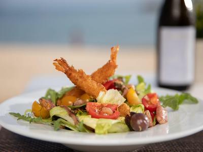 Insalata fresca con gamberi fritti, pomodori e olive su un piatto bianco in spiaggia