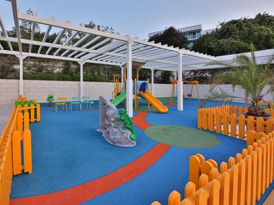 Area giochi colorata con scivolo, roccia da arrampicata e recinzione arancione in hotel