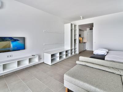 Stanza d'hotel luminosa arredata con TV, letto e zona soggiorno su pavimento piastrellato.