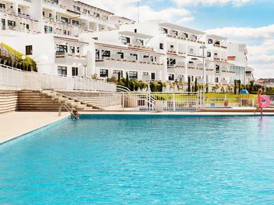 Grande piscina blu di fronte a edifici alberghieri bianchi sotto un cielo parzialmente nuvoloso.